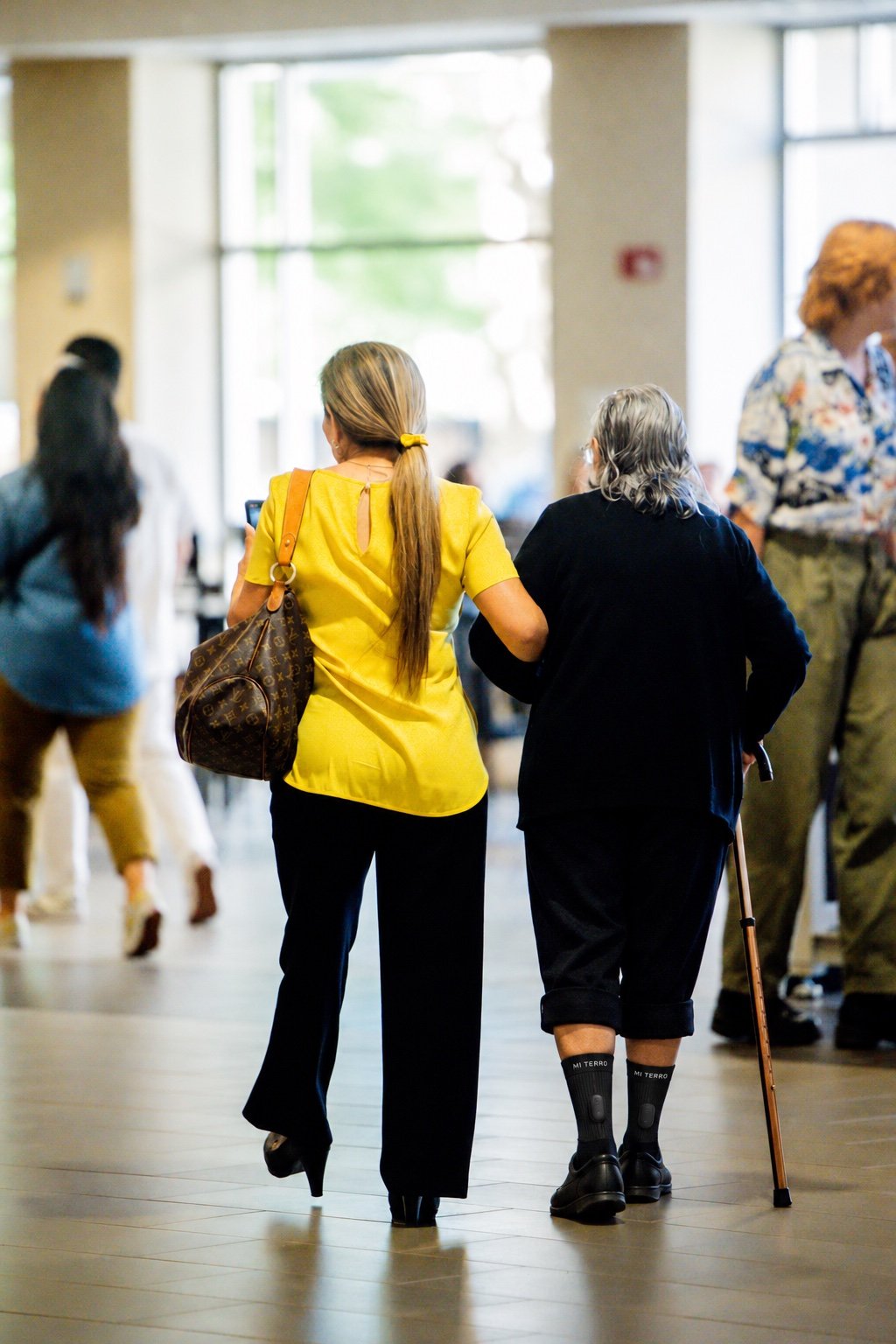 Older woman walking with caregiver support; Mi Terro Smart Socks digitally visualized on her lower legs
